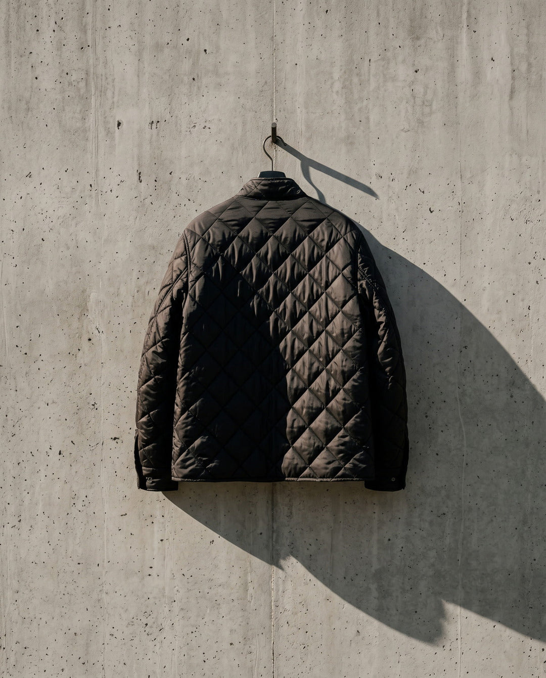 Man's black quilted jacket hanging against a concrete wall