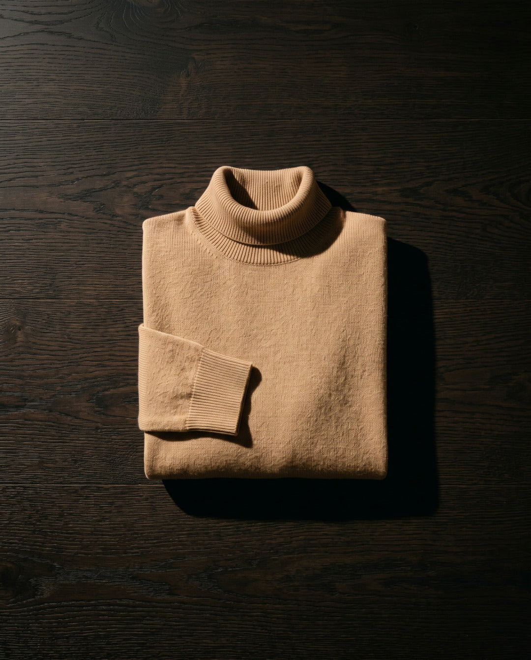 Folded camel roll-neck sweater on a dark oak surface