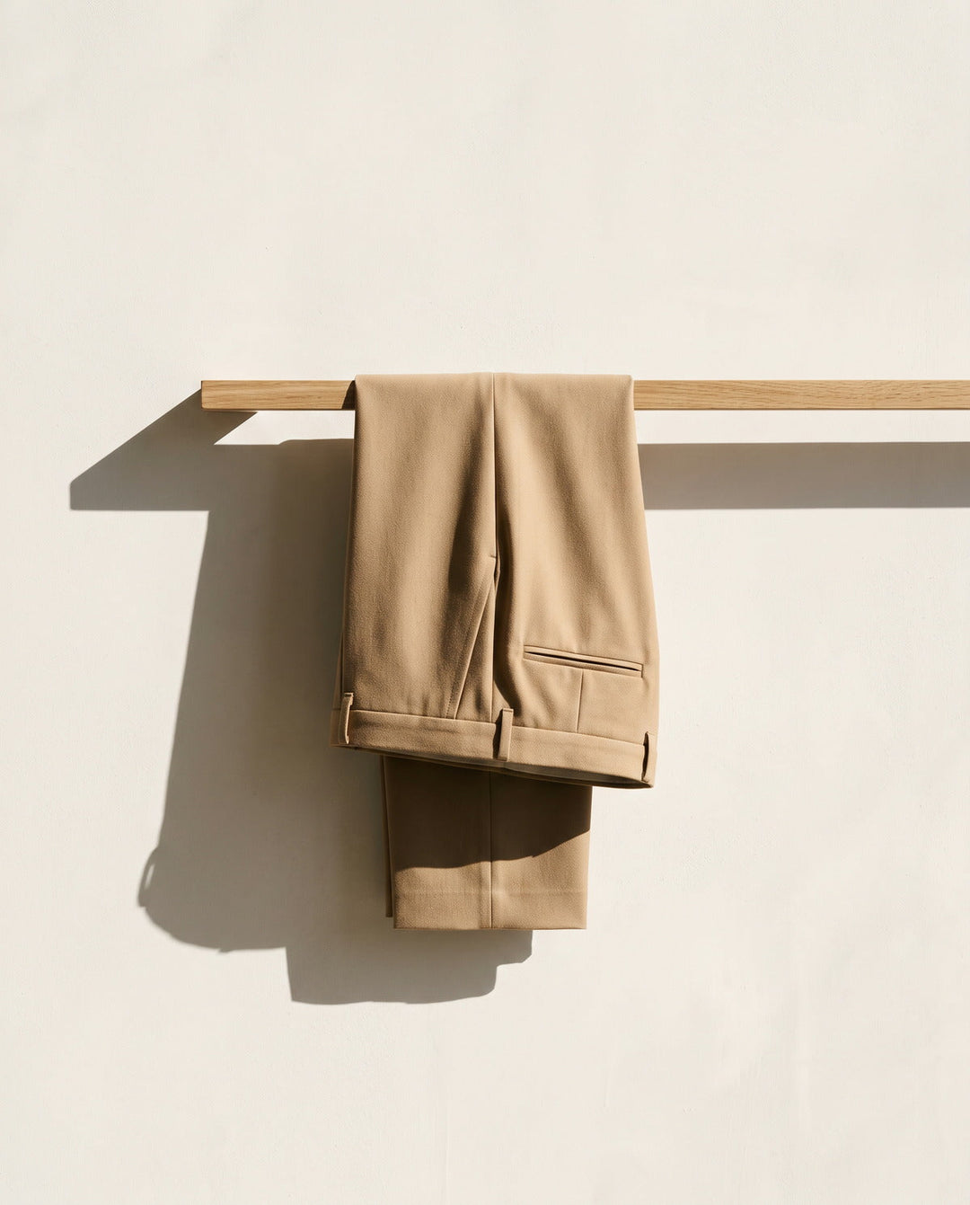 Pair of sand tailored trousers folded over a wooden rail