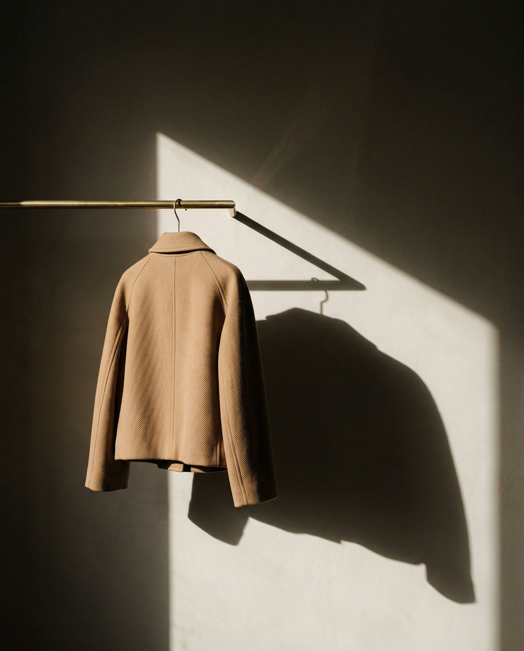 Woman's camel wool jacket hanging on a slim brass rail
