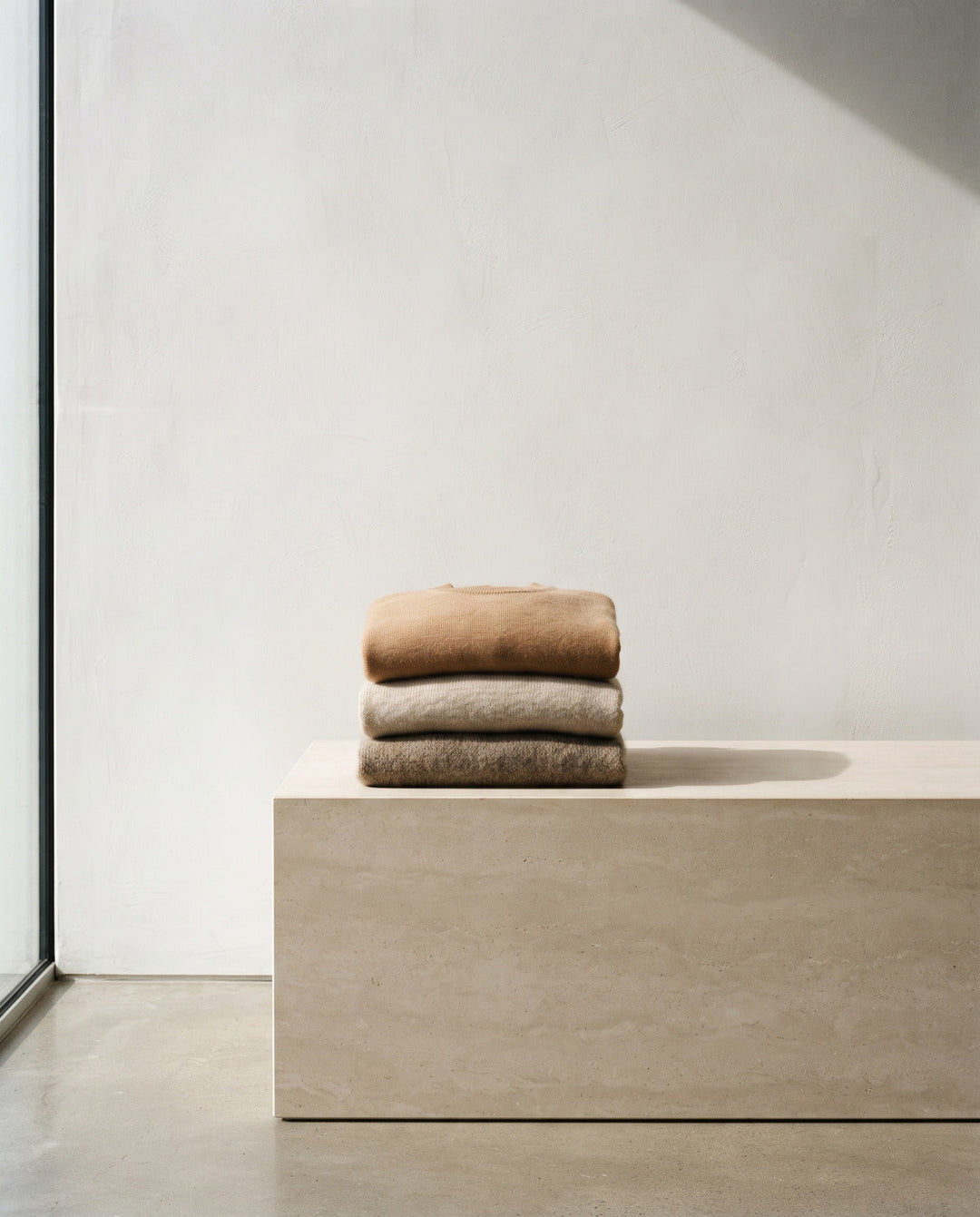 Stack of folded oatmeal and camel knitwear on a stone plinth