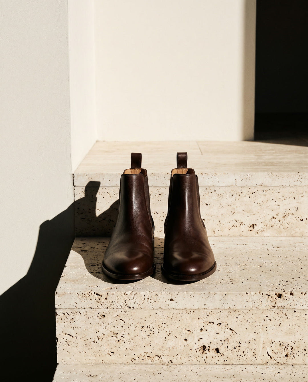 Pair of chocolate brown leather ankle boots on a travertine step