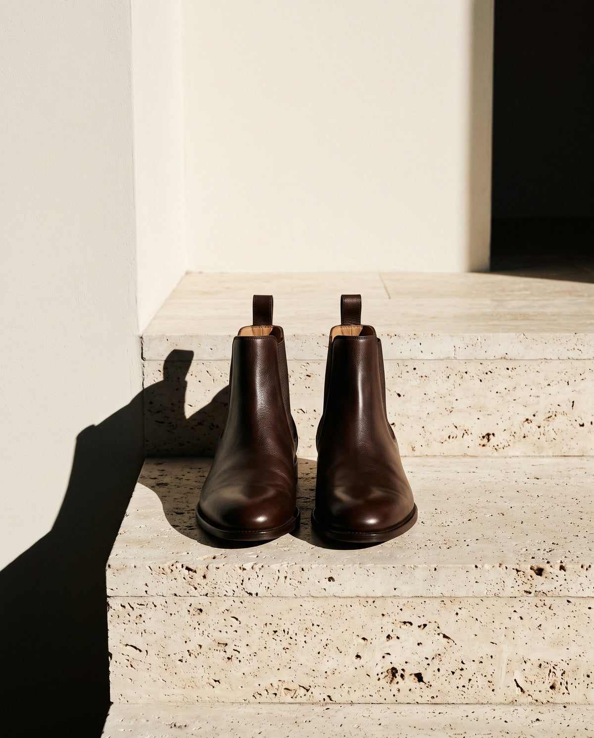 Pair of chocolate brown leather ankle boots on a travertine step