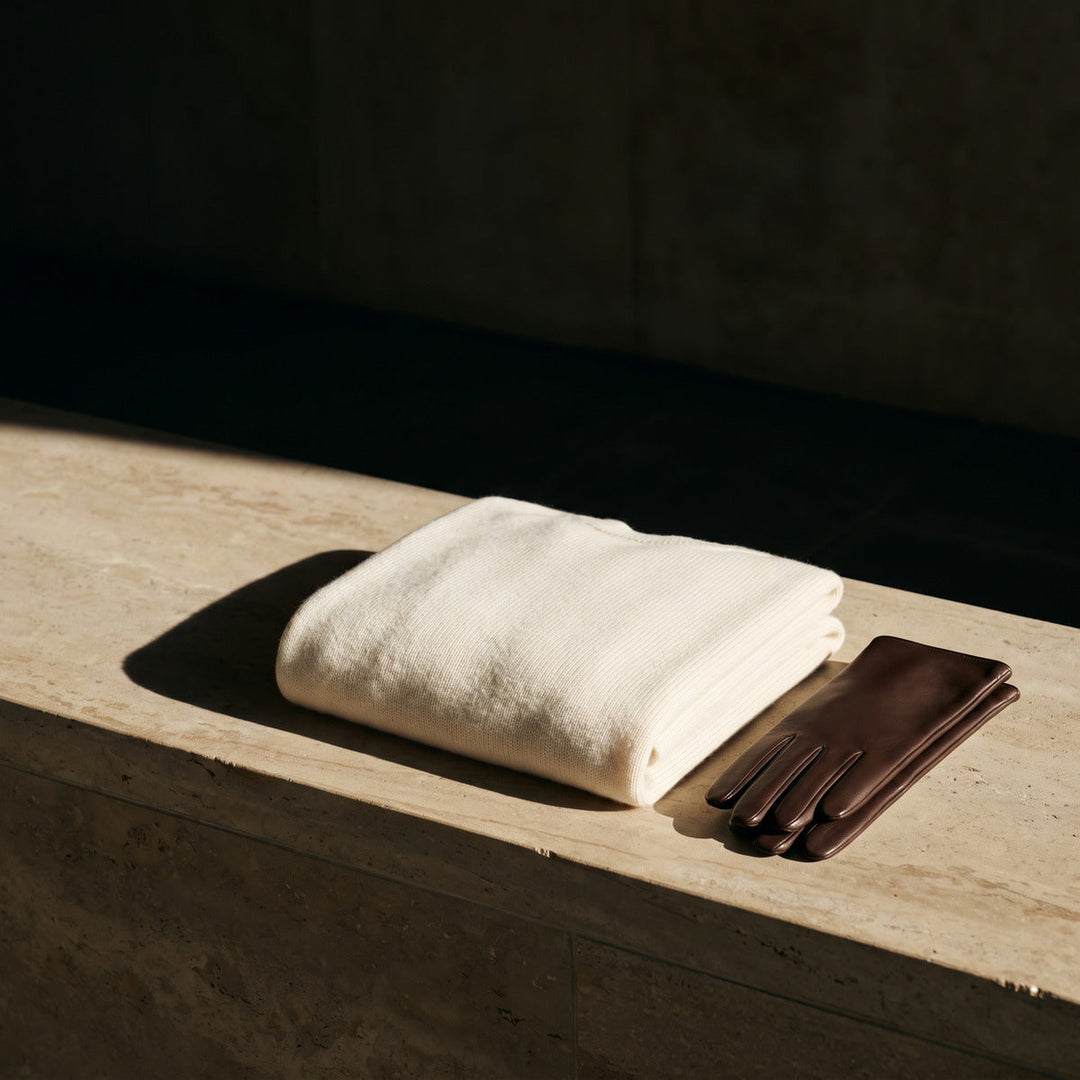 Folded ivory cashmere knit and leather gloves on a sand-coloured stone ledge